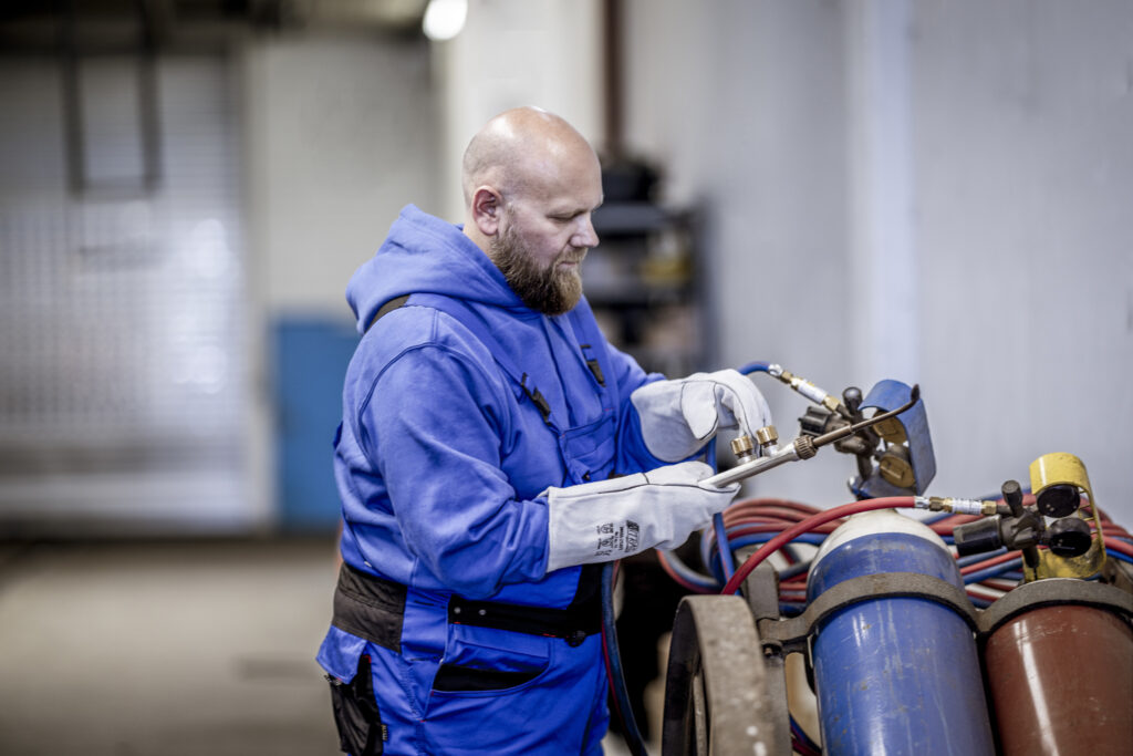 Handwerker in blauer Schutzkleidung und Handschuhen arbeitet mit einer Autogenschweißanlage.