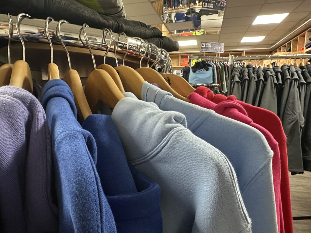 Hoodies in verschiedenen Farben, darunter Blau, Hellblau und Rot, hängen auf Holzbügeln im Laden von MP Berufsbekleidung.
