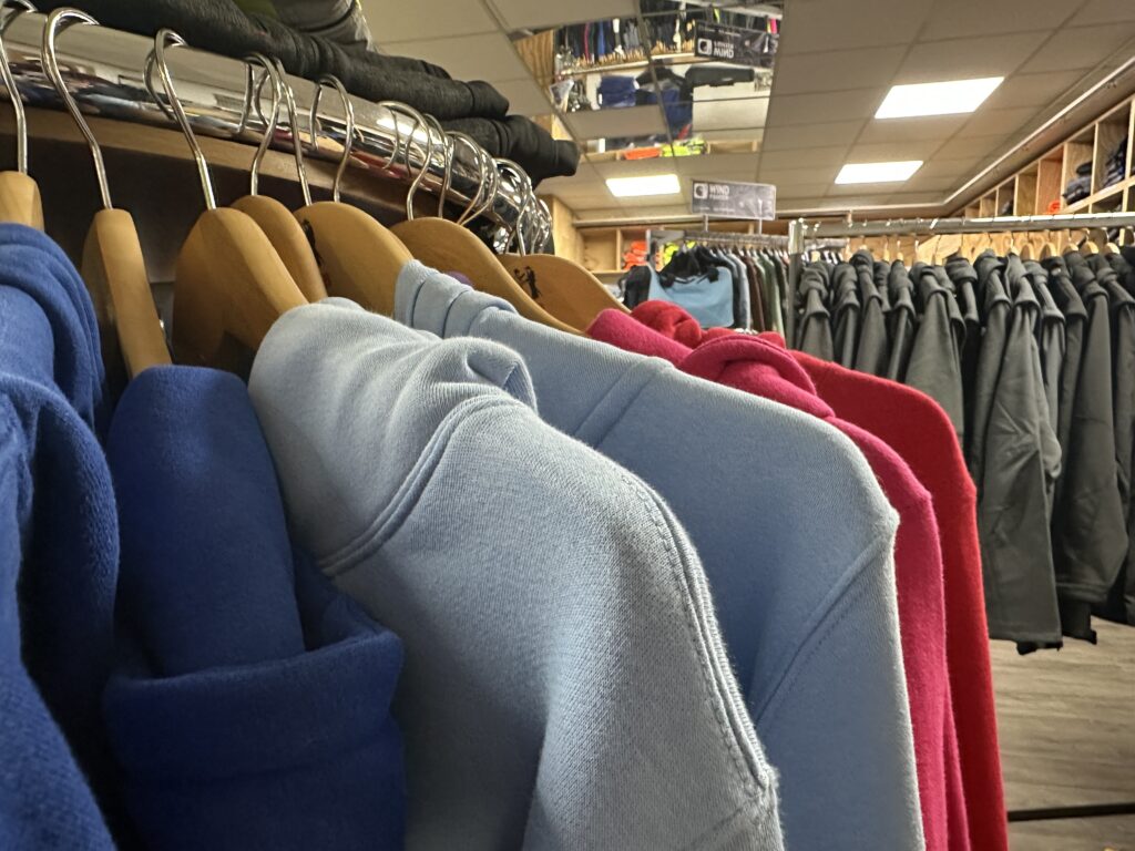 Farbig sortierte Hoodies aus dem Sortiment von MP Berufsbekleidung hängen auf Holzbügeln im Laden.