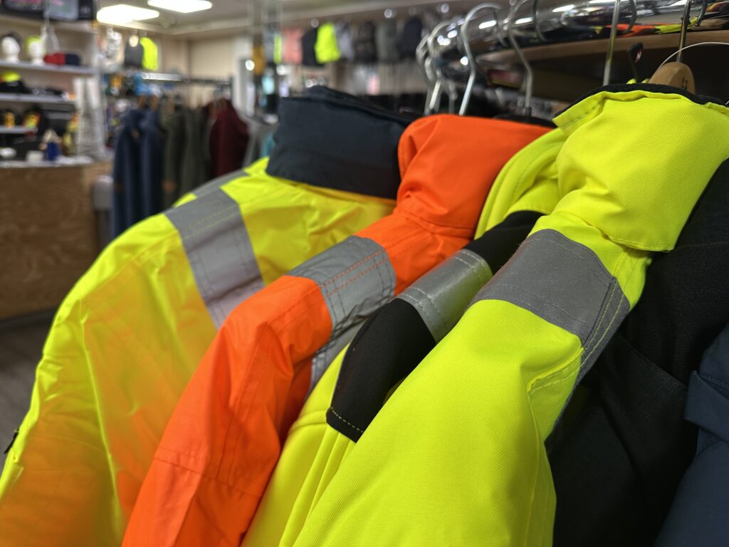 Leuchtend gelbe und orangefarbene Warnschutzjacken mit reflektierenden Streifen hängen in der Verkaufsfläche von MP Berufsbekleidung.