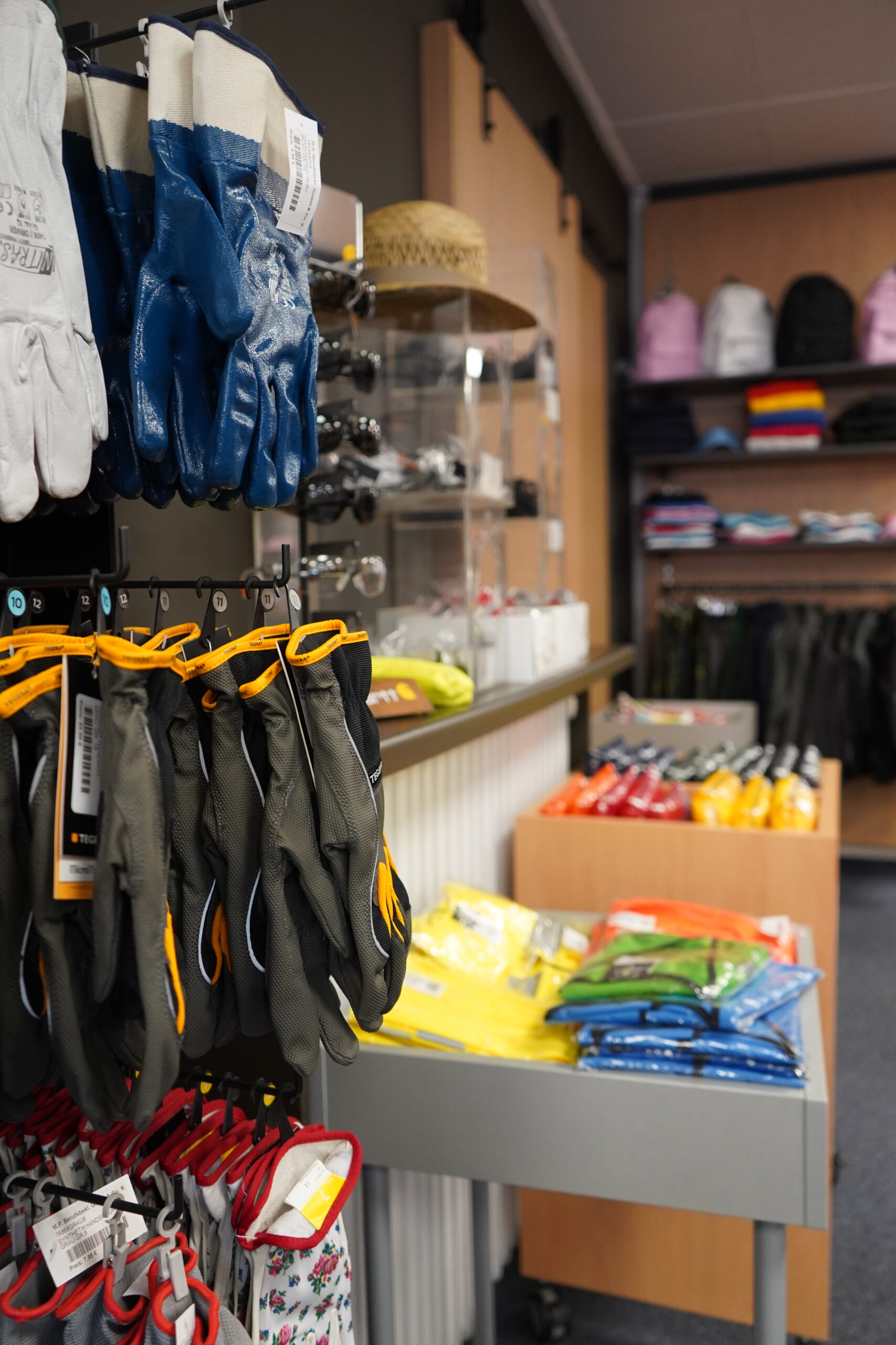 Verschiedene Arbeitshandschuhe und Schutzkleidung im Verkaufsbereich von MP Berufsbekleidung.