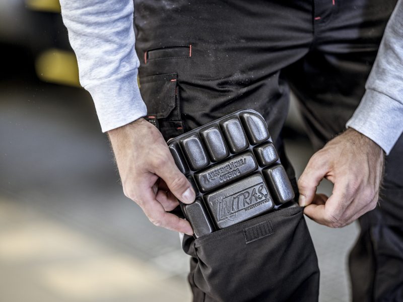 Arbeiter steckt eine schwarze NITRAS-Knieschoner-Einlage in die Kniepolstertasche seiner schwarzen Arbeitshose.