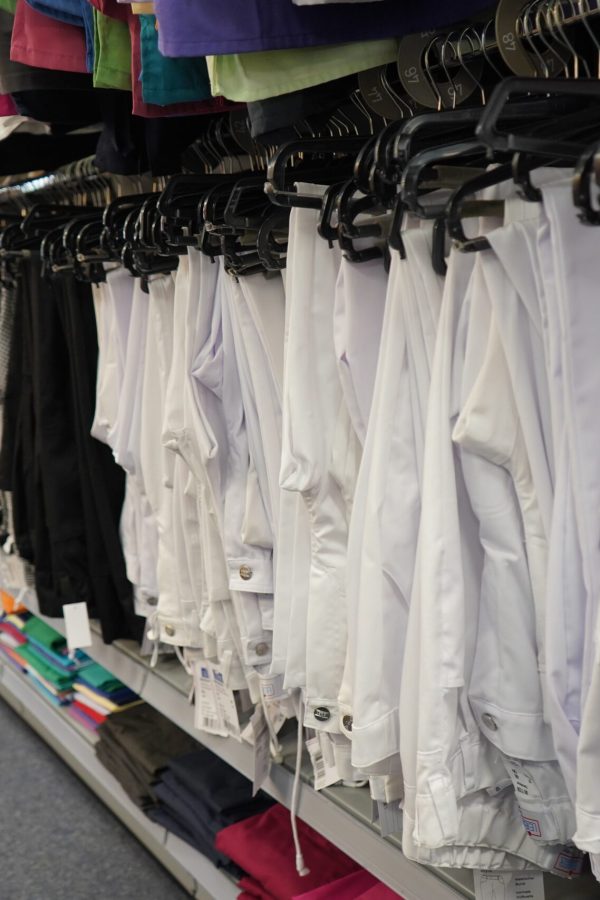 Weiße Arztkittel und Hosen auf Kleiderbügeln in einem Fachgeschäft für Berufsbekleidung.