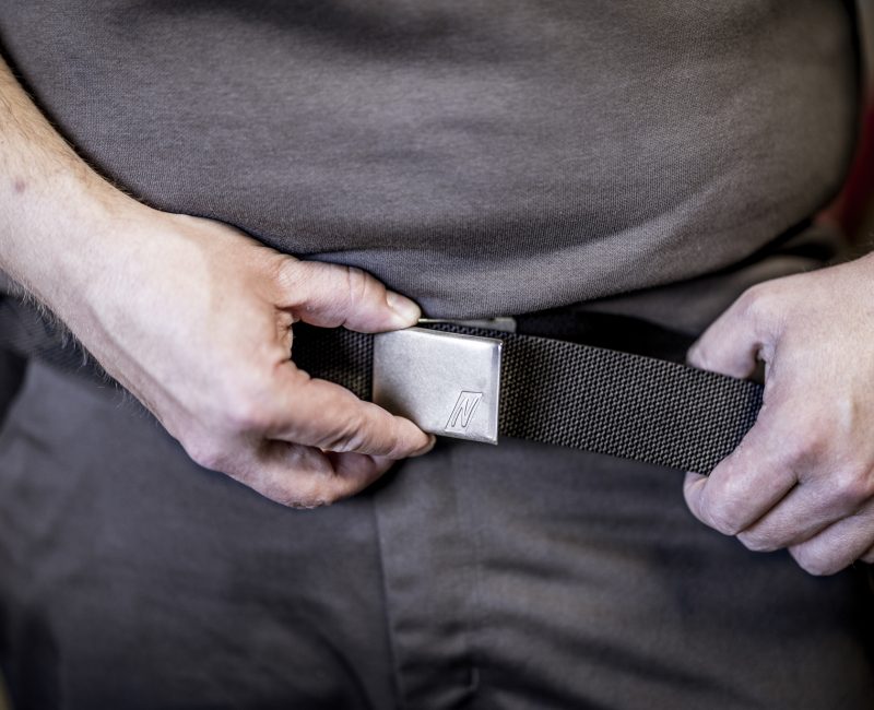 Detailaufnahme eines Arbeiters, der einen robusten schwarzen Gürtel mit Metallschnalle schließt.