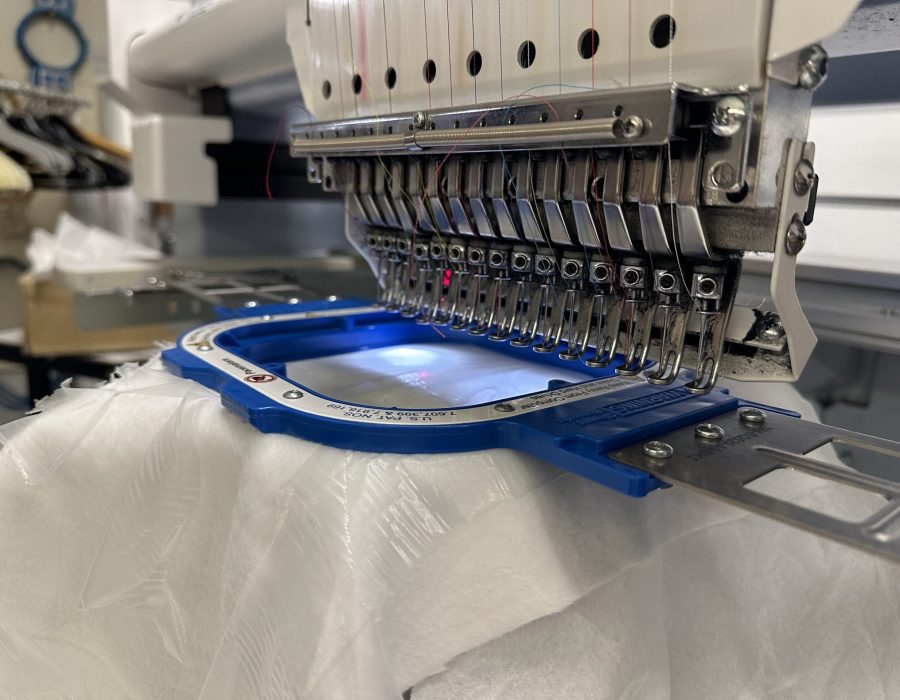 Professionelle Mehrkopf-Stickmaschine mit einem blauen Stickrahmen und eingespanntem Stoff, bereit für den Stickvorgang.