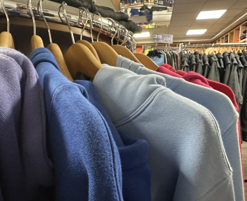 Hoodies in verschiedenen Farben, darunter Blau, Hellblau und Rot, hängen auf Holzbügeln im Laden von MP Berufsbekleidung.